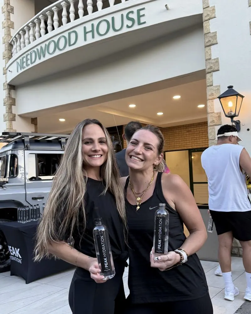 Two women holding Peak Hydration outside Heedwood House