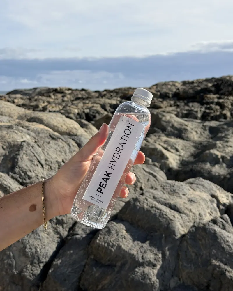 A bottle of Peak Hydration held against ancient coastal rock